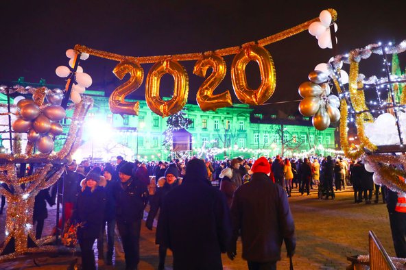 An outdoor night-time celebration of the New Year 2020 with a crowd of people and golden balloons spelling "2020" in the foreground.